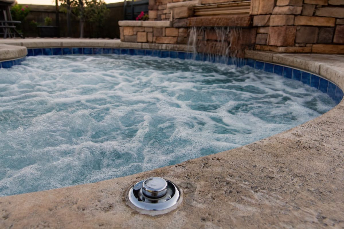 Bubbling jets in a tiled in-ground hot tub with an air control knob on the stone deck