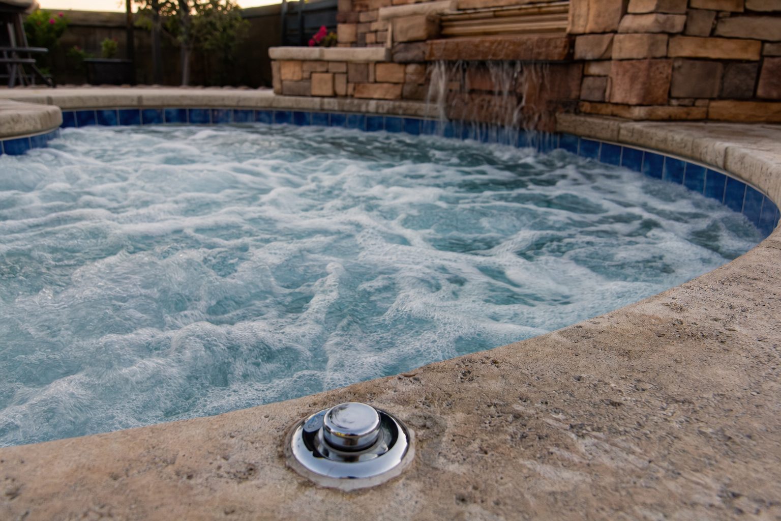 Bubbling jets in a tiled in-ground hot tub with an air control knob on the stone deck