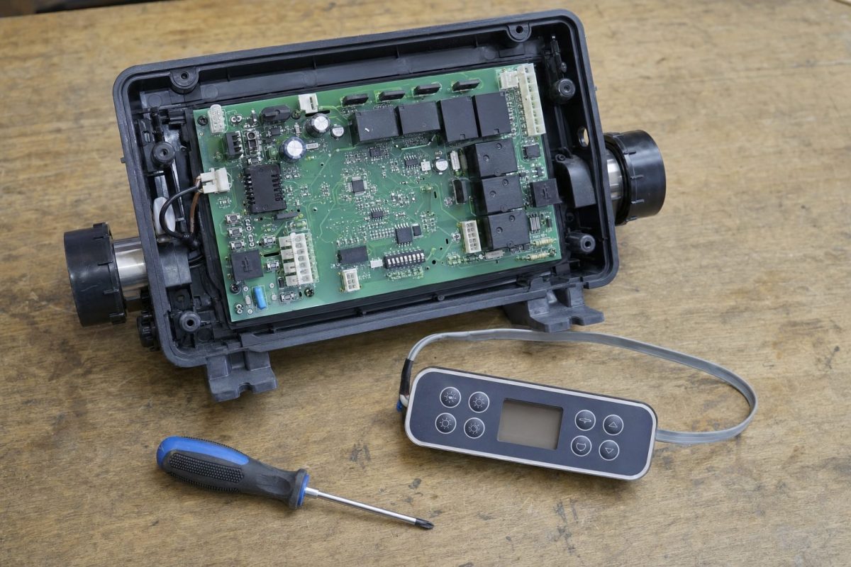 Balboa spa pack with its front cover off on a workbench, showing the circuit board and DIP switches