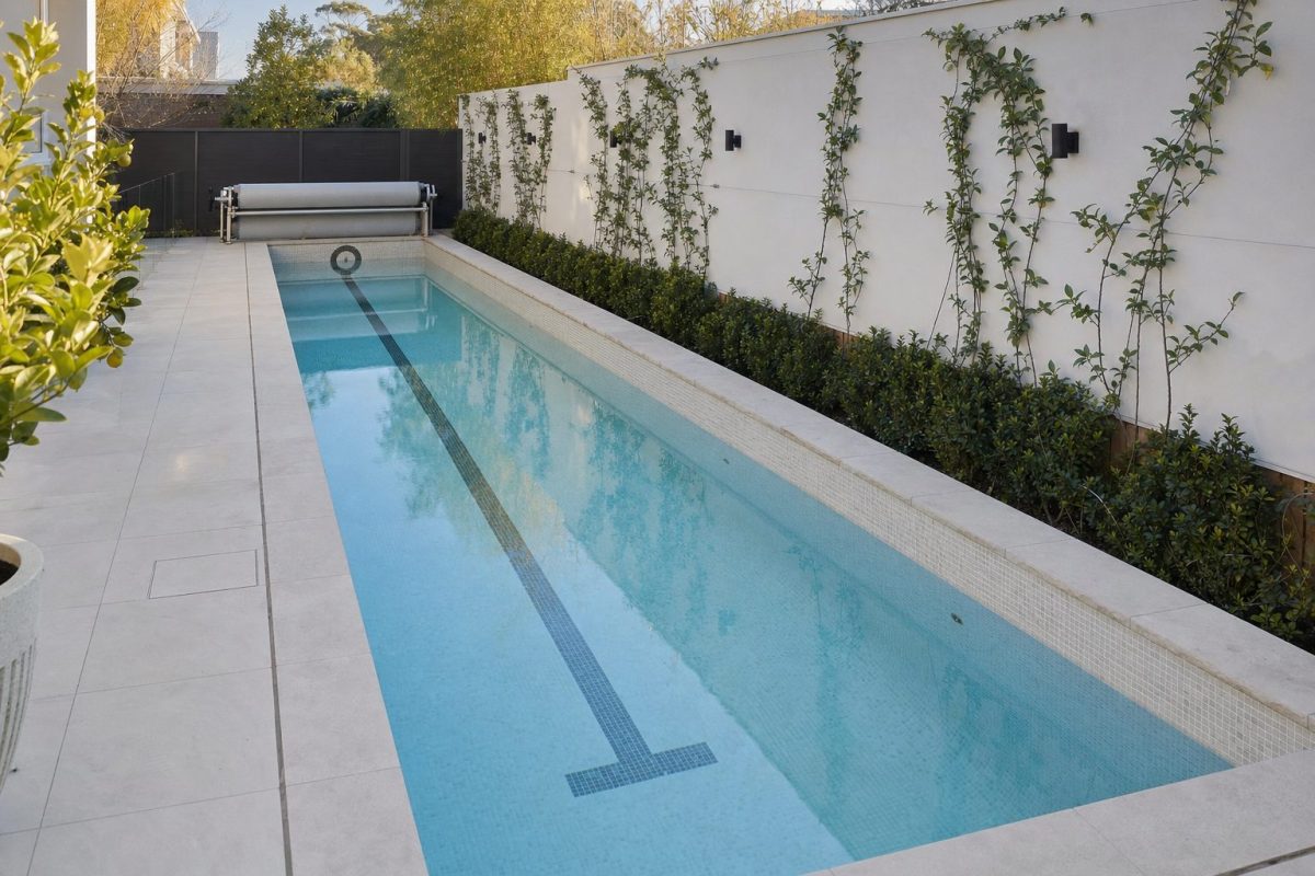 Long, narrow DIY in-ground lap pool with a tiled lane line along a garden boundary