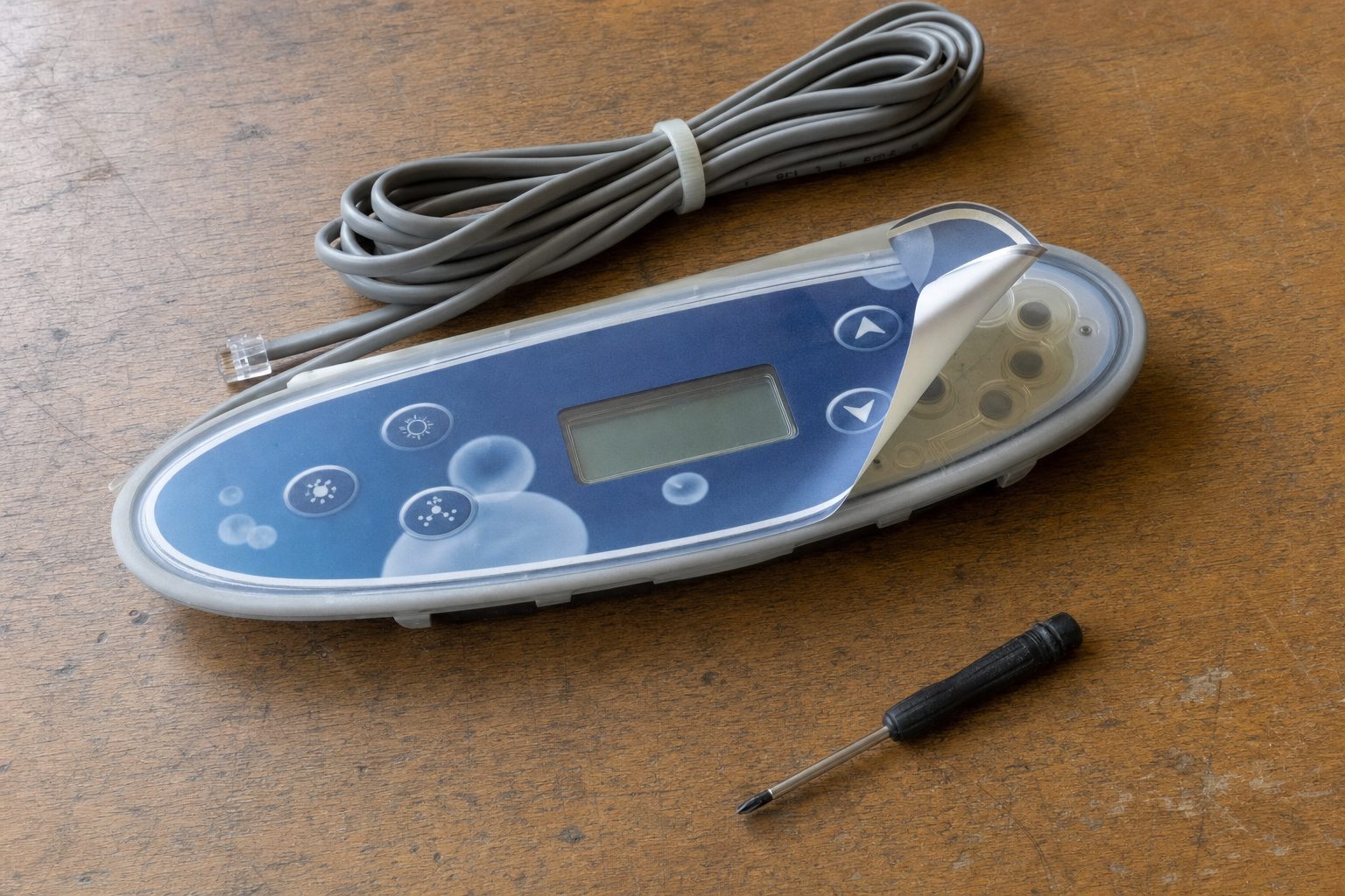 Hot tub topside control panel with its printed overlay partly peeled back on a workbench