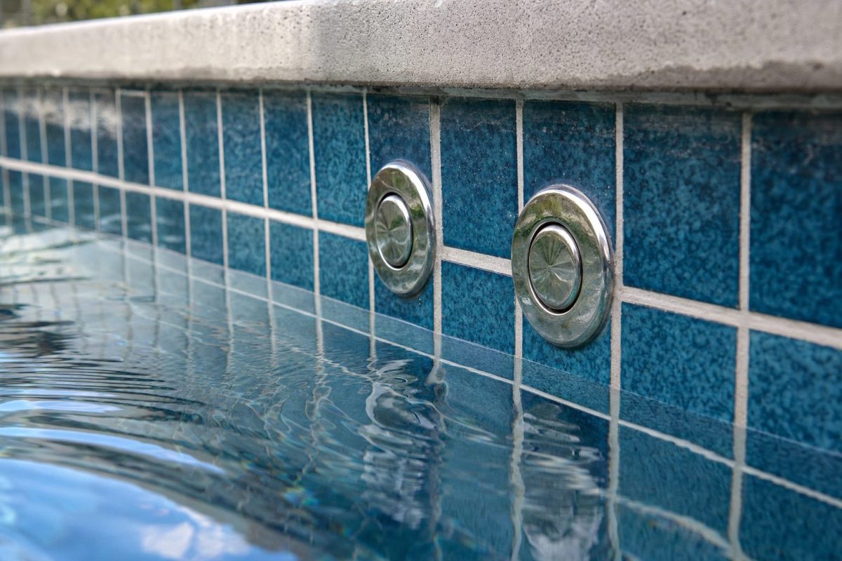 Chrome hot tub air button set into a tiled spa wall above the waterline