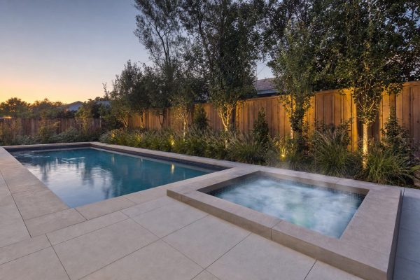 A tiled in-ground plunge pool beside a smaller steaming in-ground hot tub in a landscaped back garden