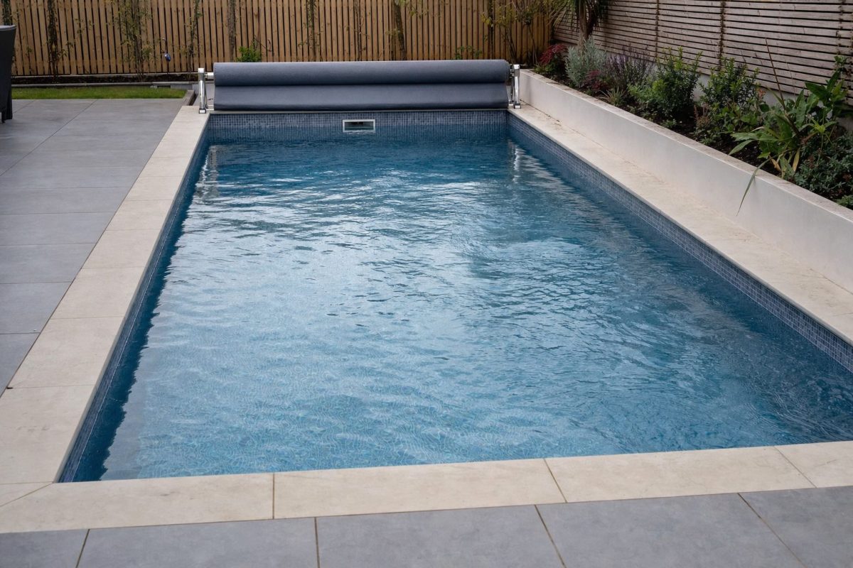 DIY in-ground exercise pool with a counter current swim jet, tiled interior and stone coping in a back garden