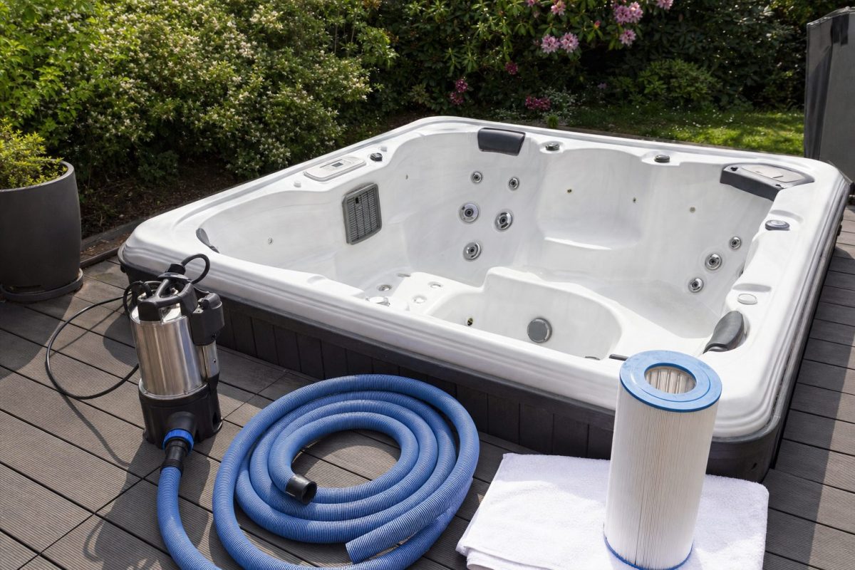 Drained hot tub shell with a submersible pump, hose and a clean filter drying on a towel