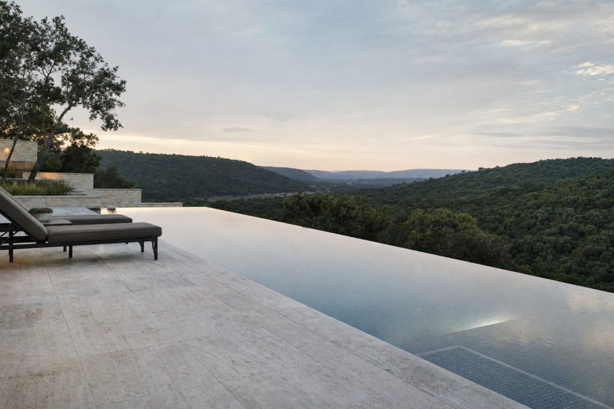 Infinity edge swimming pool with water spilling over the far edge towards a countryside view